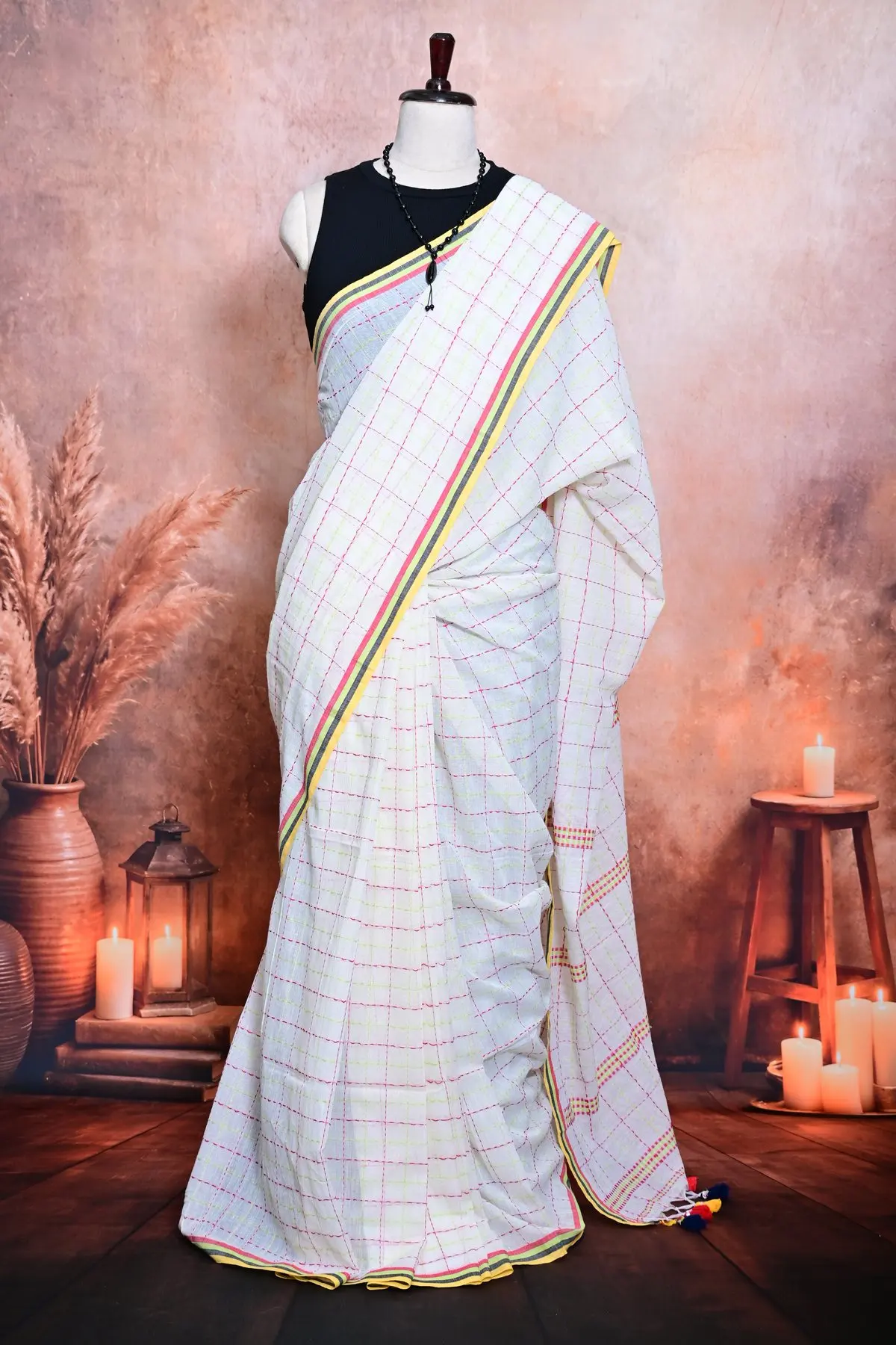 Close view of a white cotton saree in pleats, with fine pink and lime checks and a yellow, green and red striped border.