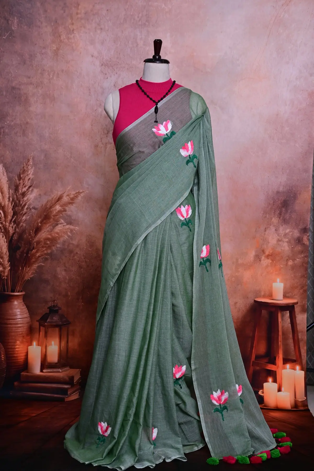 Sage green cotton saree in soft pleats, embroidered with pink and white lotus flowers.