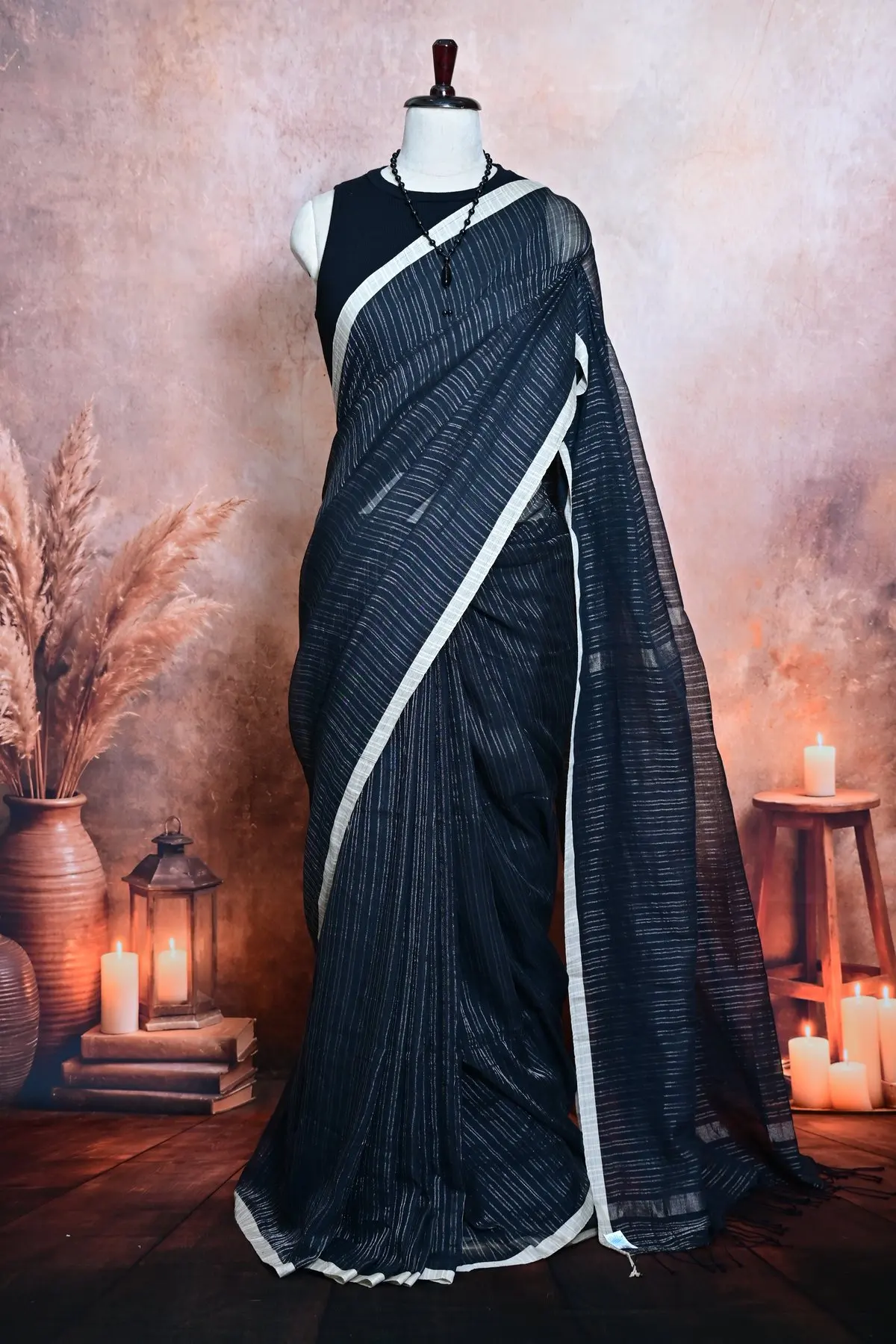 Close view of a blue-black cotton saree with fine silver pinstripes and an off-white border across the drape.