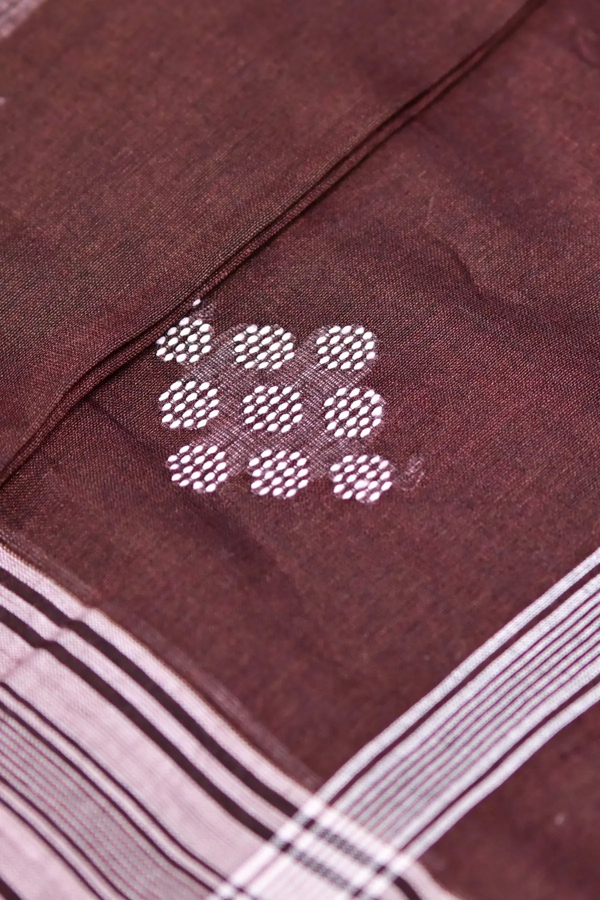 Maroon saree fabric gathered in folds, with white stripes and clusters of round dotted motifs.