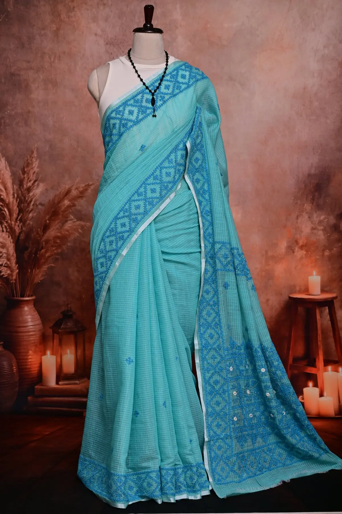 Aqua checked saree in pleats, with small blue motifs, a blue diamond border at the hem and the embroidered pallu beside it.
