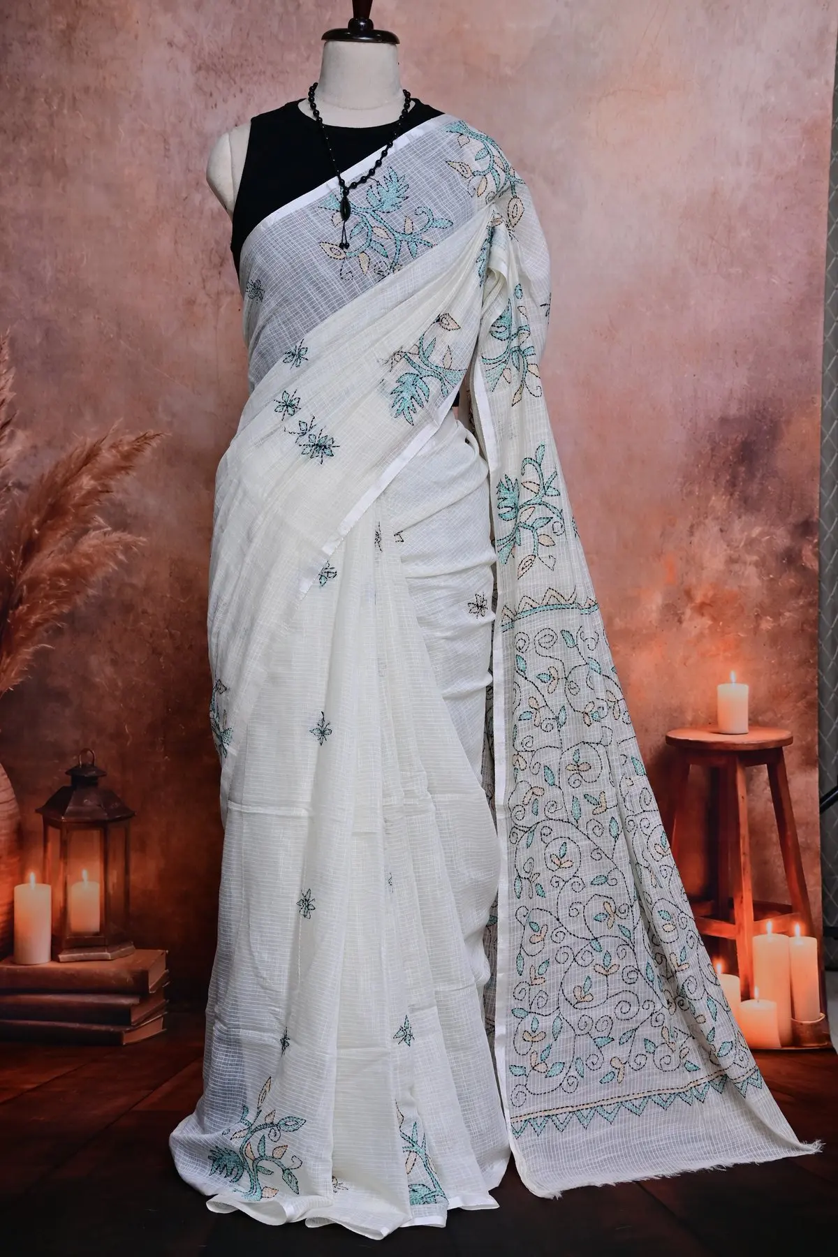 Off-white checked saree in pleats beside a pallu embroidered with teal and peach leaves on black vines.