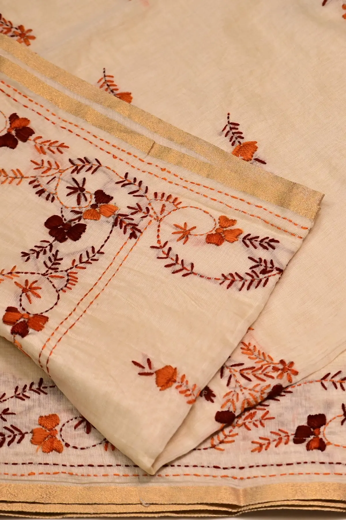 Cream saree in soft folds, with a rust and maroon embroidered flower spray and a vine border along the top.