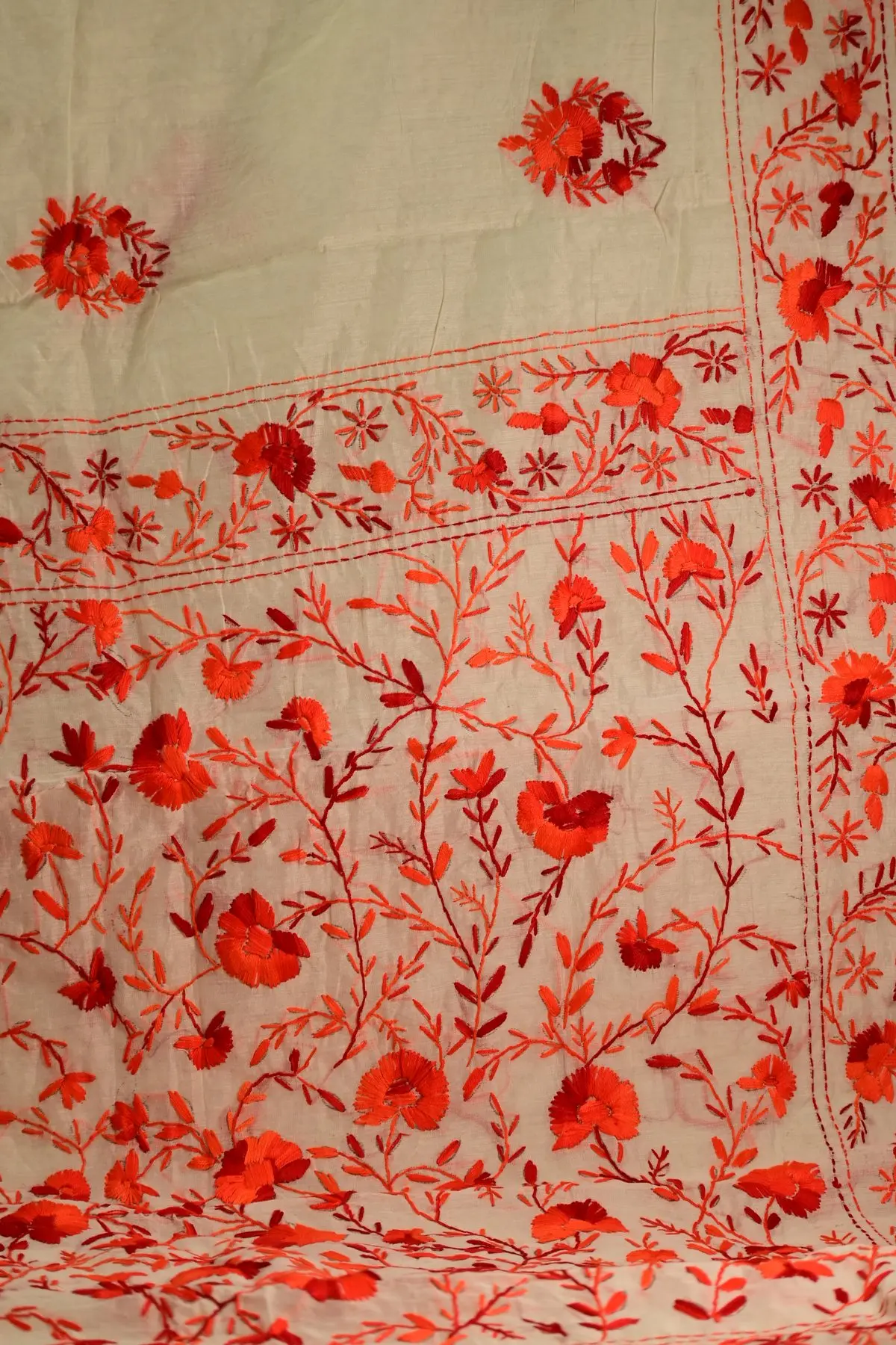 Ivory saree hung flat to show its pallu of red floral vines, framed by an embroidered floral border.