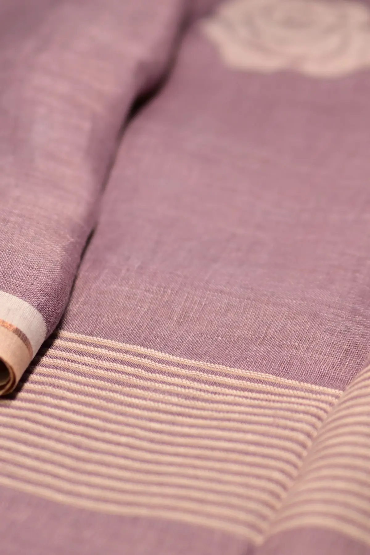 A mauve linen saree gathered into a swirl, with an off-white rose motif at the centre.