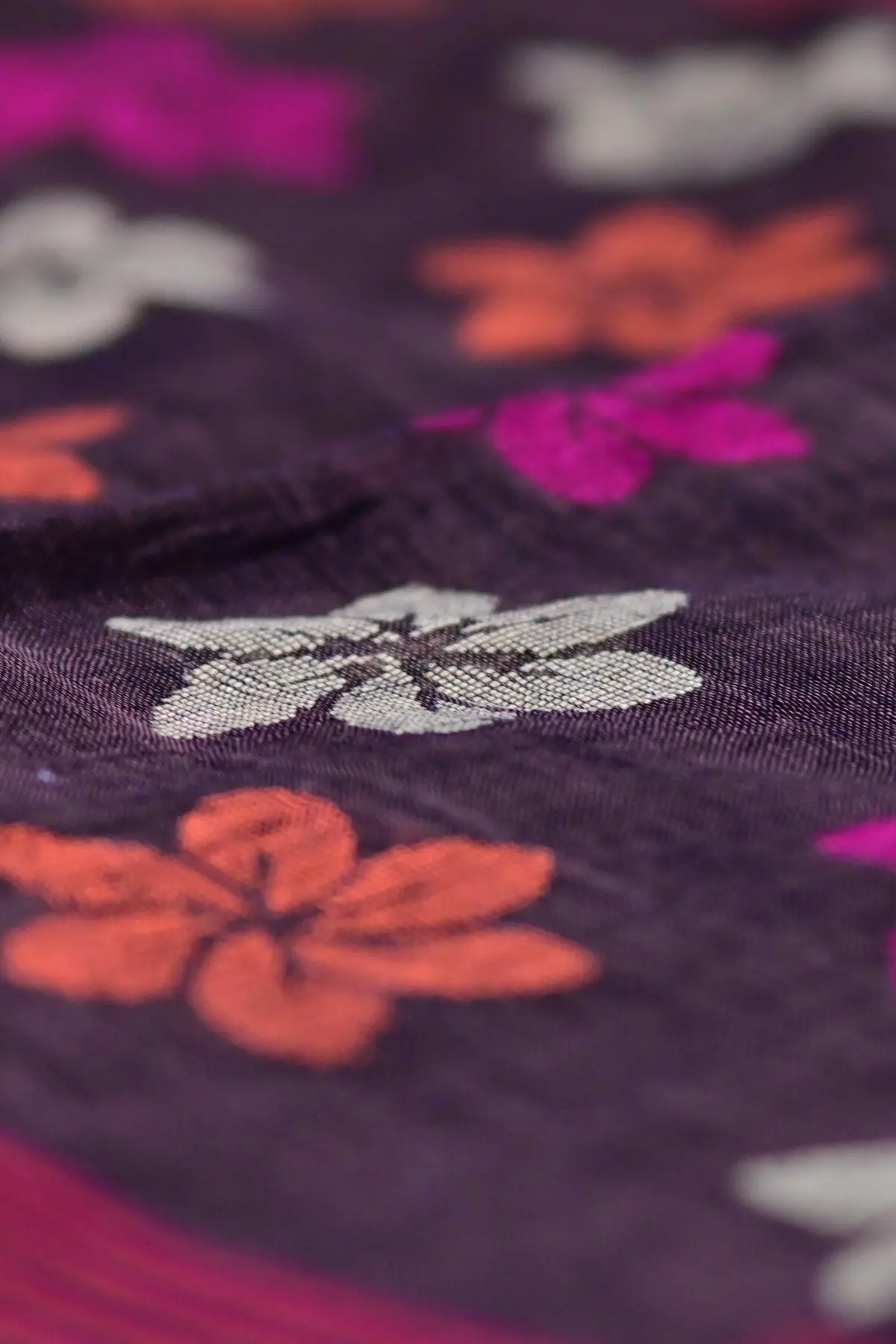 A deep aubergine linen saree swirled to show flower motifs in magenta, orange and beige.