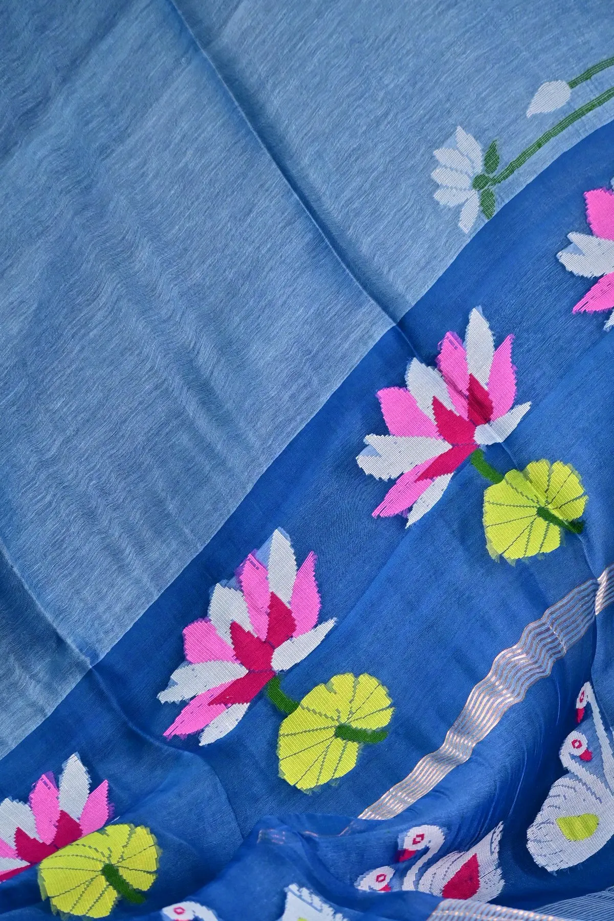 Close-up of a blue linen saree pallu with a pink lotus, a lime lily pad and a white swan.